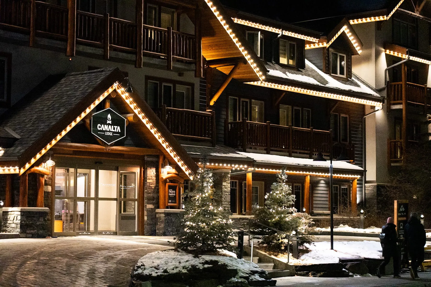 Timber-frame lodge in winter with warm white permanent lights along the rooflines