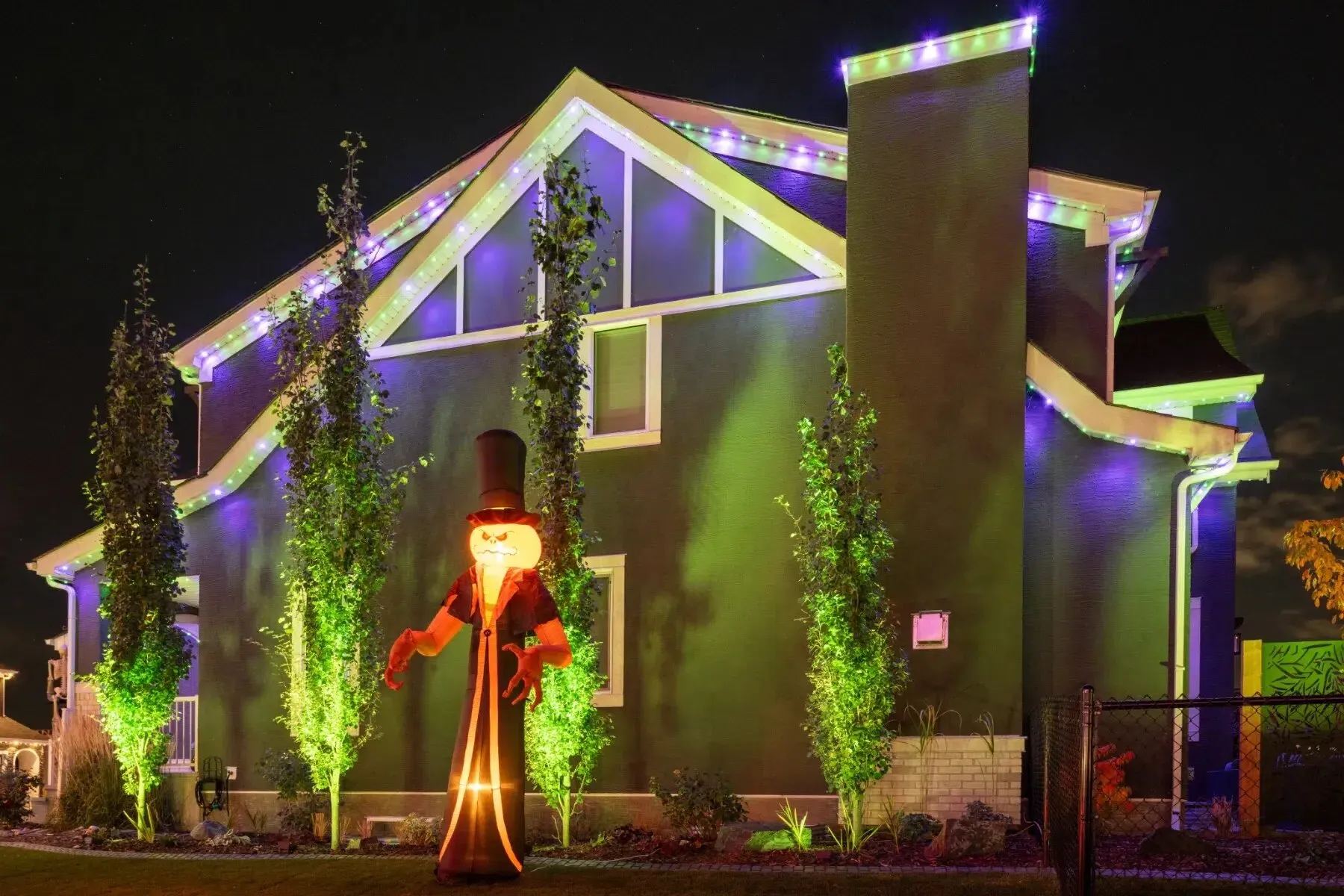 Home with purple roofline lights and green uplighting on trees for Halloween