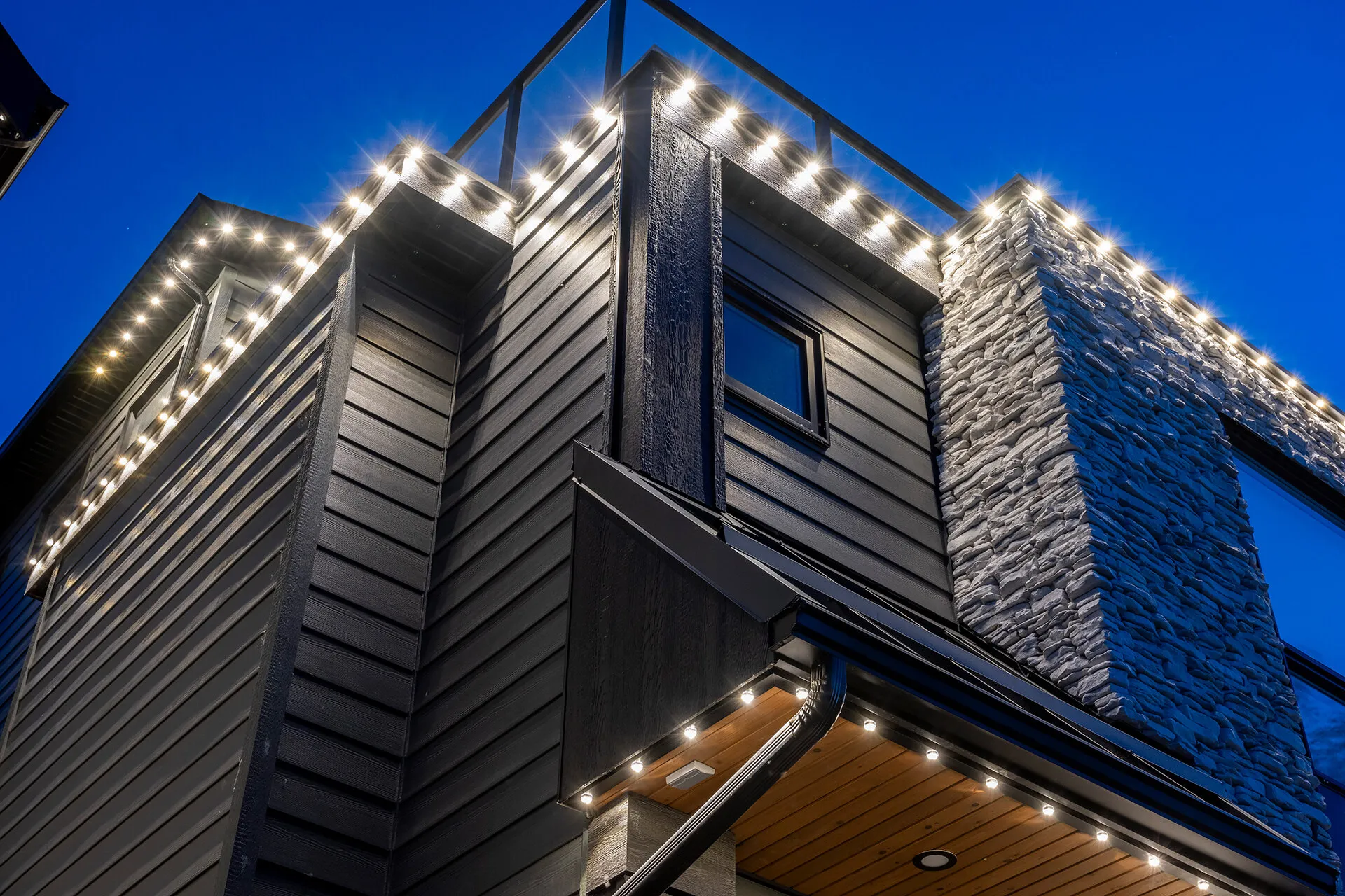 Close view of bright white lights along the soffit of a stone-and-siding home