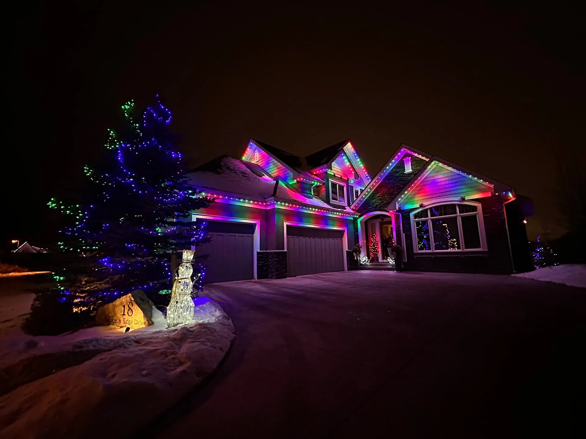 Home with multicolour permanent Christmas lights at night with snow on the ground