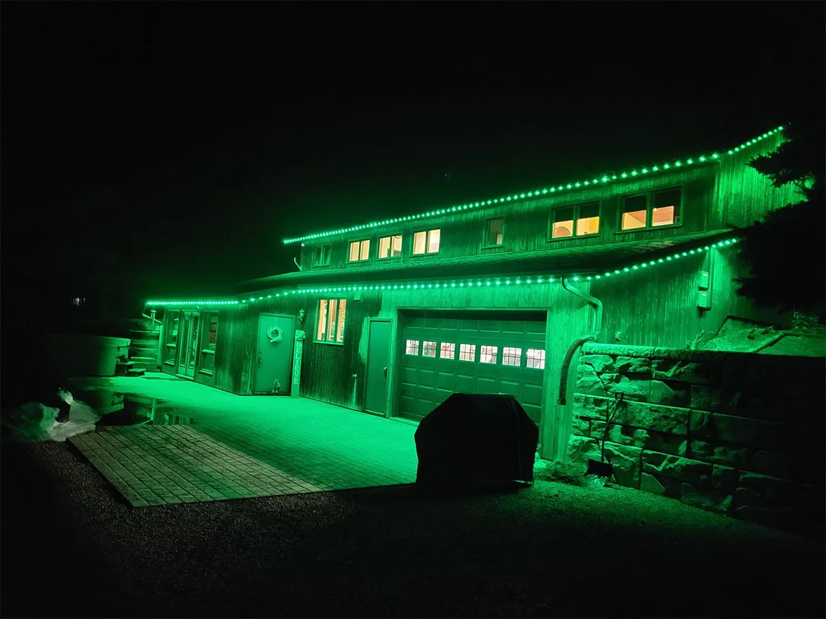 Home with green permanent roofline lights on a snowy winter night