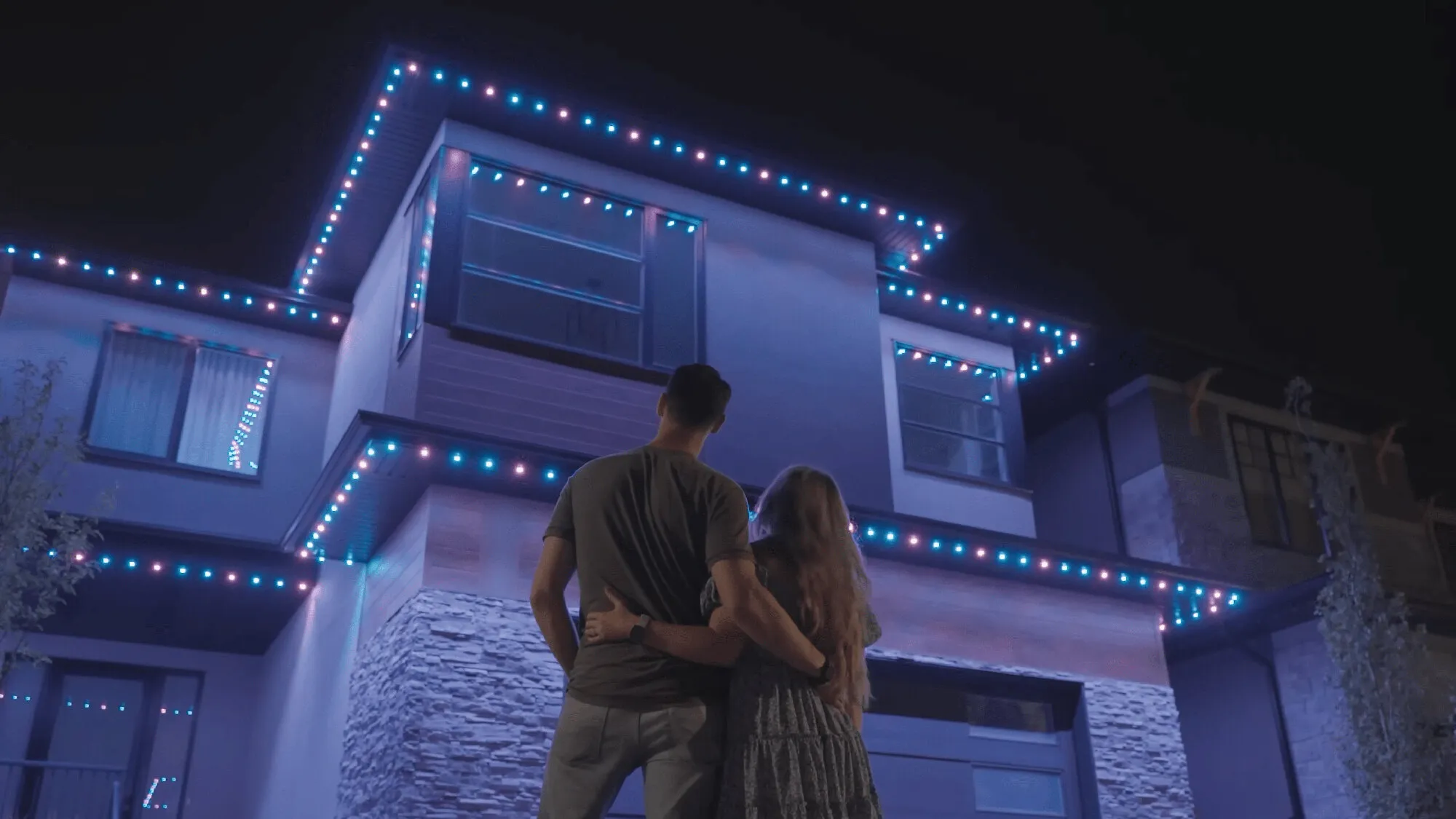 Couple in front of a modern home with blue and white permanent lights
