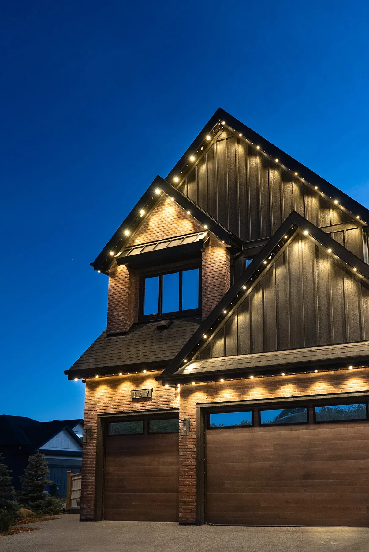 Two-storey home with warm white lights tracing every gable at blue hour